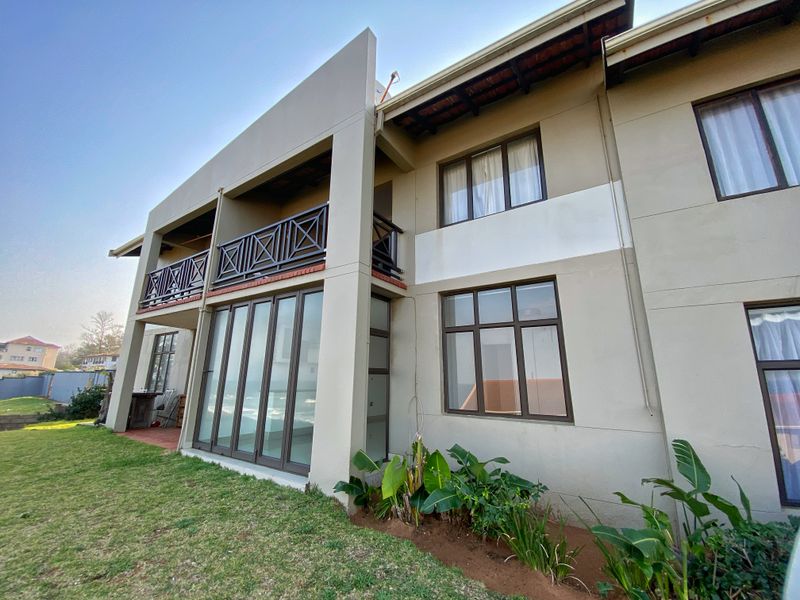 Rear elevation of the apartment building featuring a balcony, large sliding glass doors, and established garden area.
