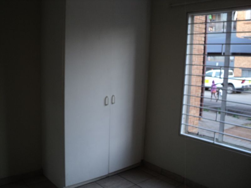 A simple bedroom featuring a built-in cupboard and a window fitted with security bars.