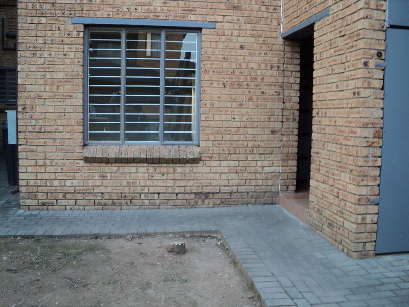 Rear exterior view of the apartment featuring a face brick facade, security-barred window, and a paved walkway leading to the entrance.