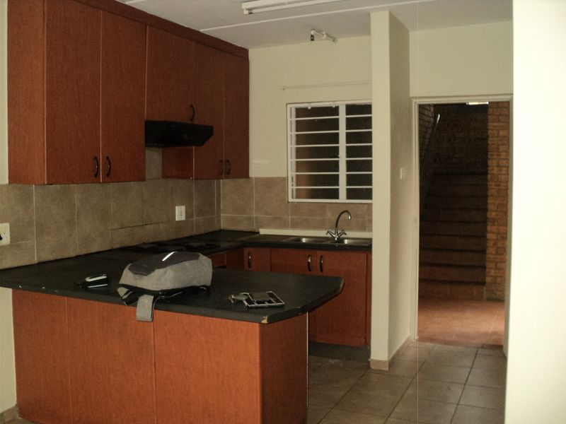 A functional kitchen featuring laminate cabinetry, dark countertops, a tiled backsplash, and a stainless steel sink with a view toward an adjacent stairwell.