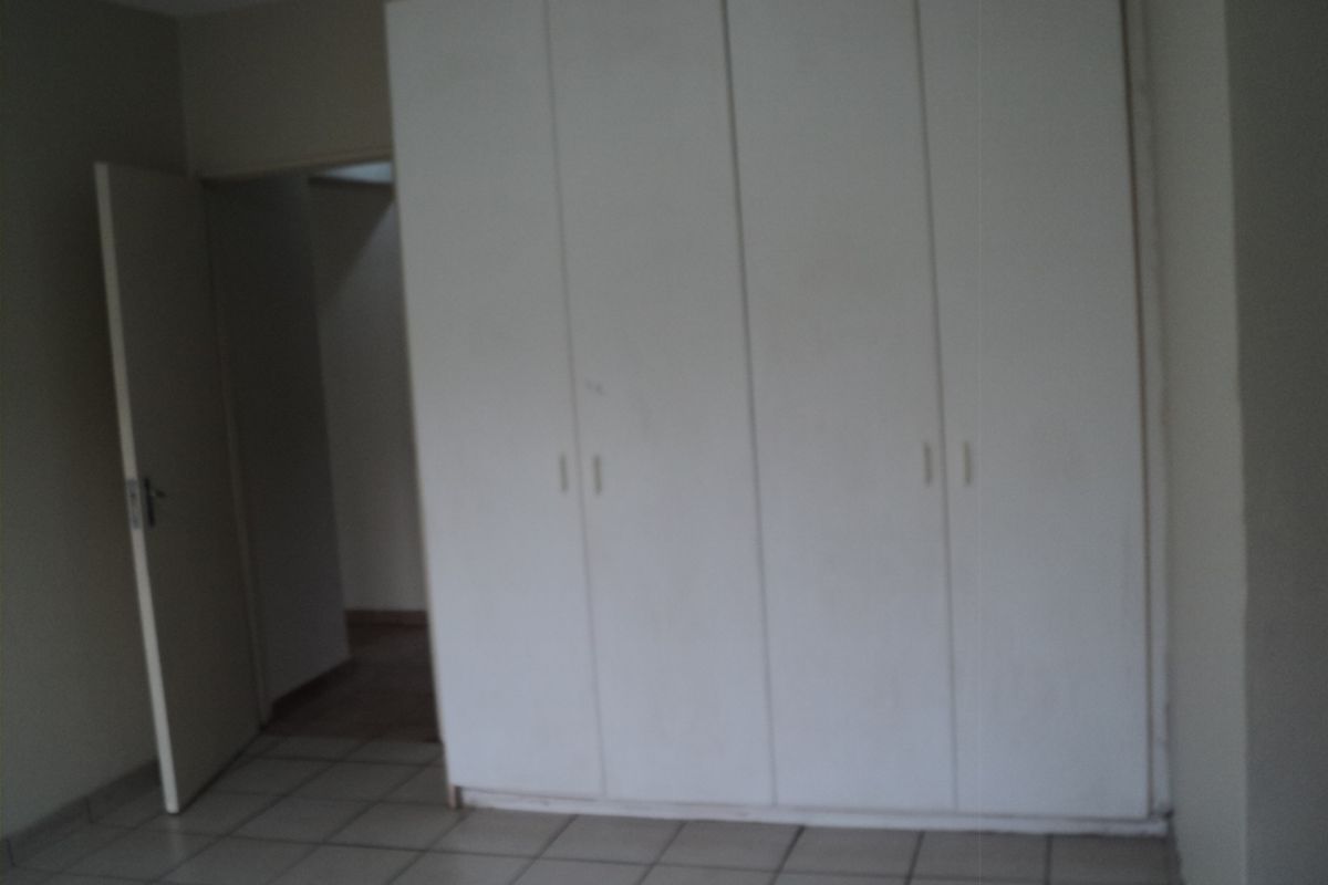 A vacant bedroom featuring neutral tiled flooring and built-in white cupboards, offering a clean and functional space ready for personalization.