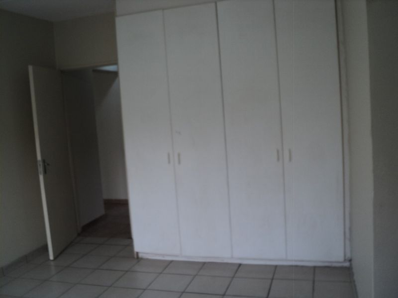 A vacant bedroom featuring neutral tiled flooring and built-in white cupboards, offering a clean and functional space ready for personalization.