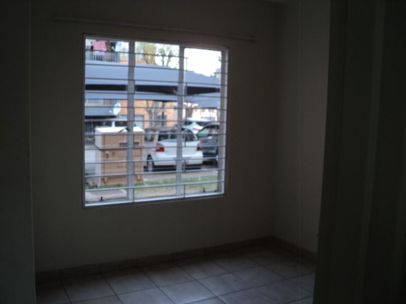 An empty bedroom featuring tiled flooring and a window fitted with security bars.