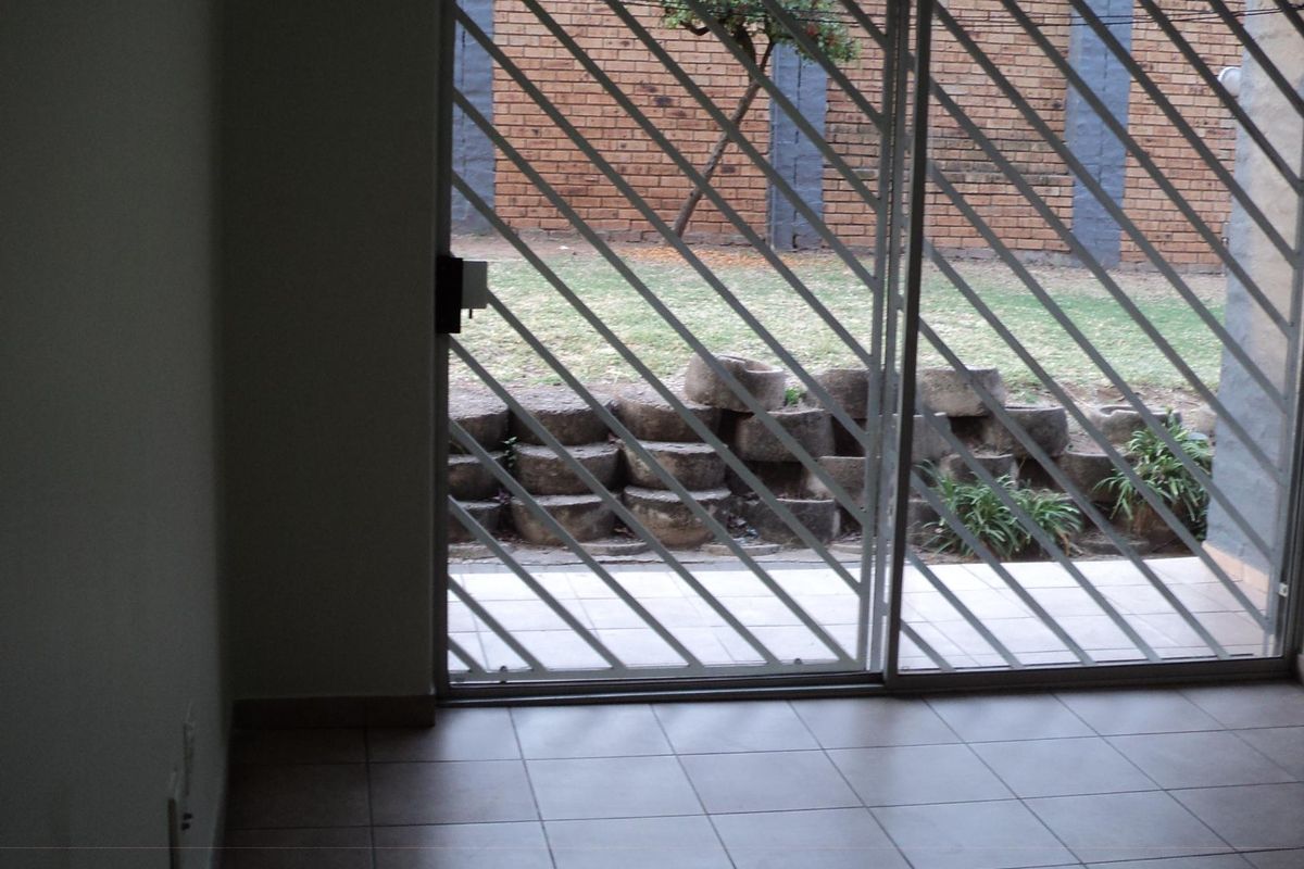 An empty living area featuring tiled flooring and a sliding glass door with a security gate, providing access to the rear garden.