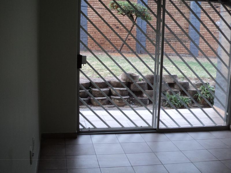 An empty living area featuring tiled flooring and a sliding glass door with a security gate, providing access to the rear garden.