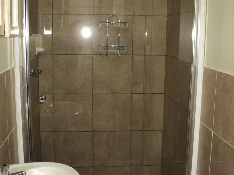 A functional bathroom featuring a tiled shower enclosure with a glass door and a pedestal basin with a mixer tap.