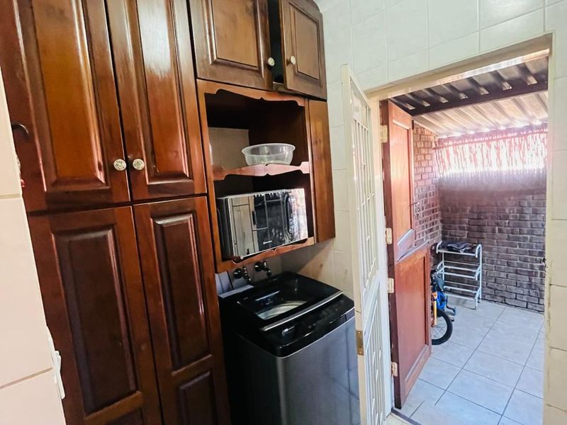 A functional laundry area featuring built-in wooden cabinetry, tiled flooring, and direct access to an outdoor courtyard space.