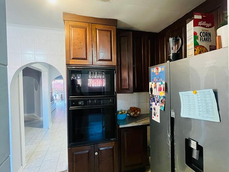 A functional kitchen featuring dark wood cabinetry, built-in oven and microwave, and tiled flooring, leading through an archway to the rest of the home.