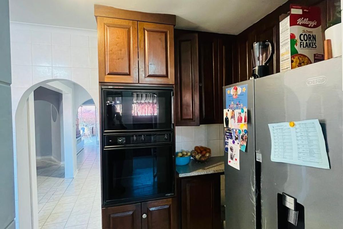 A functional kitchen featuring dark wood cabinetry, built-in oven and microwave, and tiled flooring, leading through an archway to the rest of the home.
