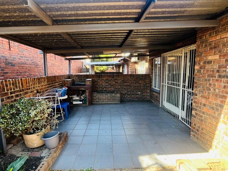 A covered outdoor patio area featuring tiled flooring, a built-in brick braai, and secure access to the main dwelling.