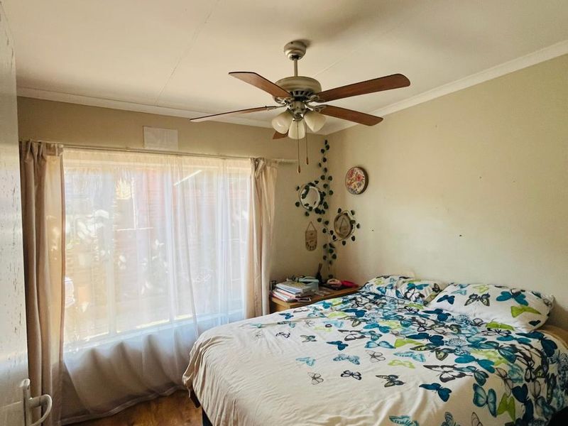 A functional bedroom featuring laminate flooring, a ceiling fan, and a large window providing natural light.