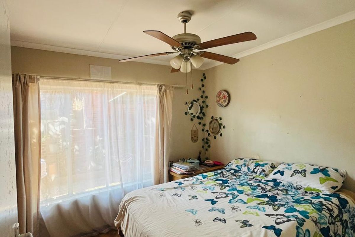 A functional bedroom featuring laminate flooring, a ceiling fan, and a large window providing natural light.