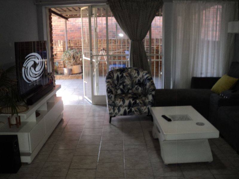 A living room featuring tiled flooring and a security gate leading to an outdoor patio area.