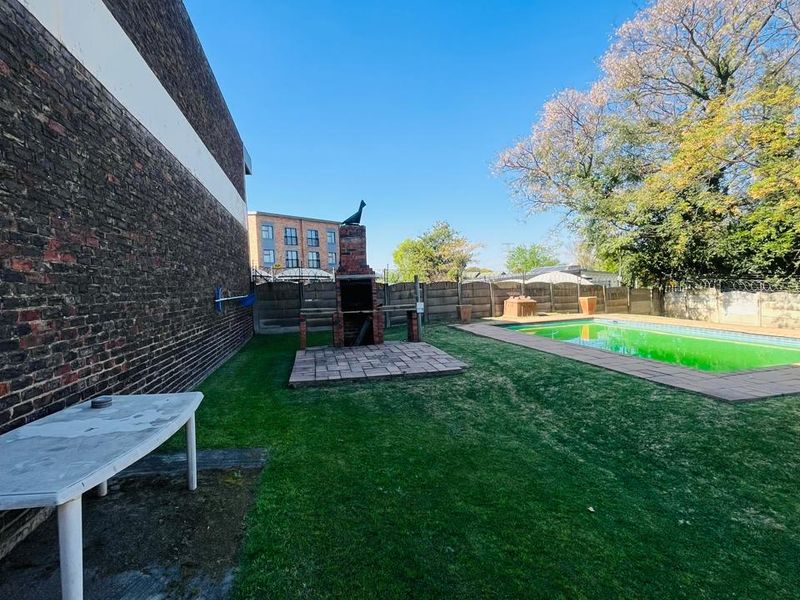Spacious backyard featuring a swimming pool, a brick built-in braai area, and a large lawn enclosed by precast concrete boundary walls.