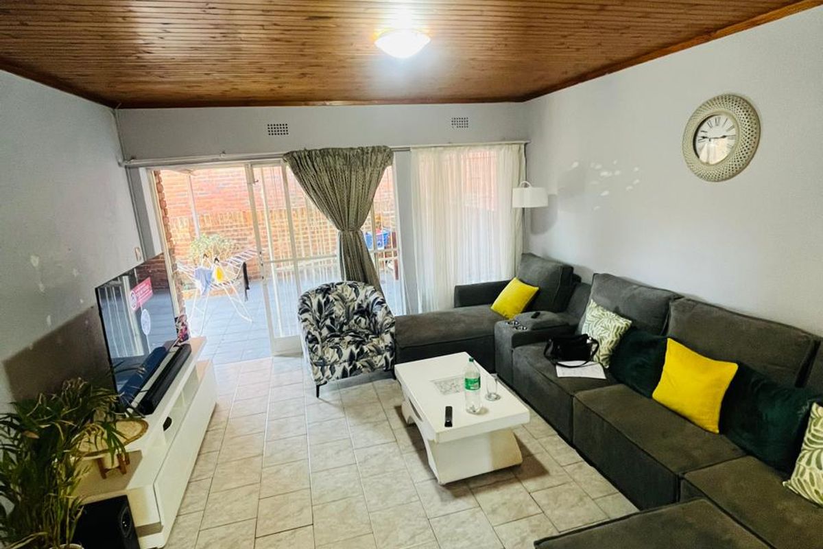 A living room featuring a timber tongue and groove ceiling, ceramic tiled flooring, and sliding glass doors providing access to the outdoor patio area.