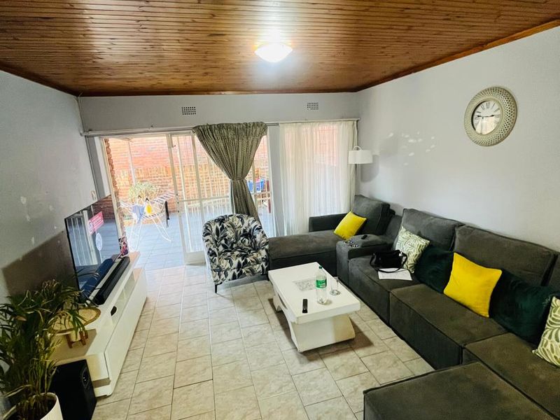 A living room featuring a timber tongue and groove ceiling, ceramic tiled flooring, and sliding glass doors providing access to the outdoor patio area.