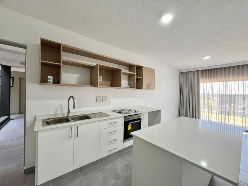 Modern kitchen featuring white cabinetry, stone countertops, a central island, built-in oven, gas hob, and open shelving, finished with neutral floor tiles.