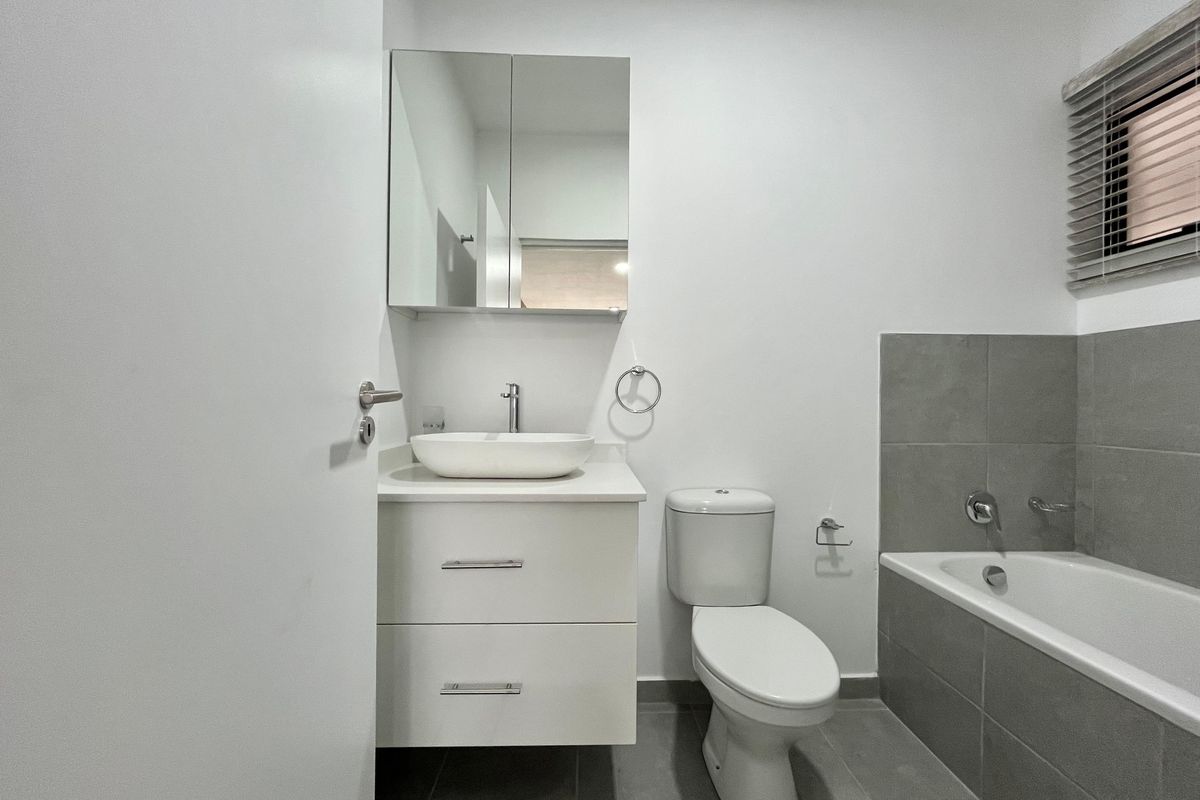 A modern, clean bathroom featuring a floating vanity with a vessel sink, a mirrored cabinet, a toilet, and a tiled bathtub surround.