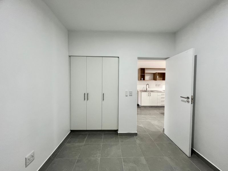 A clean, modern hallway featuring neutral tiled flooring and built-in storage cupboards, providing a seamless transition to the adjacent kitchen area.