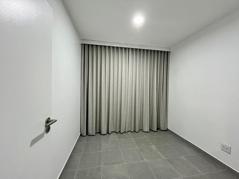 A clean, empty bedroom featuring neutral ceramic floor tiles, recessed ceiling lighting, and full-length curtains, providing a blank canvas for personalization.