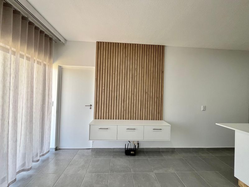 A modern living area featuring a contemporary timber slat feature wall, wall-mounted white cabinetry, and neutral tiled flooring.