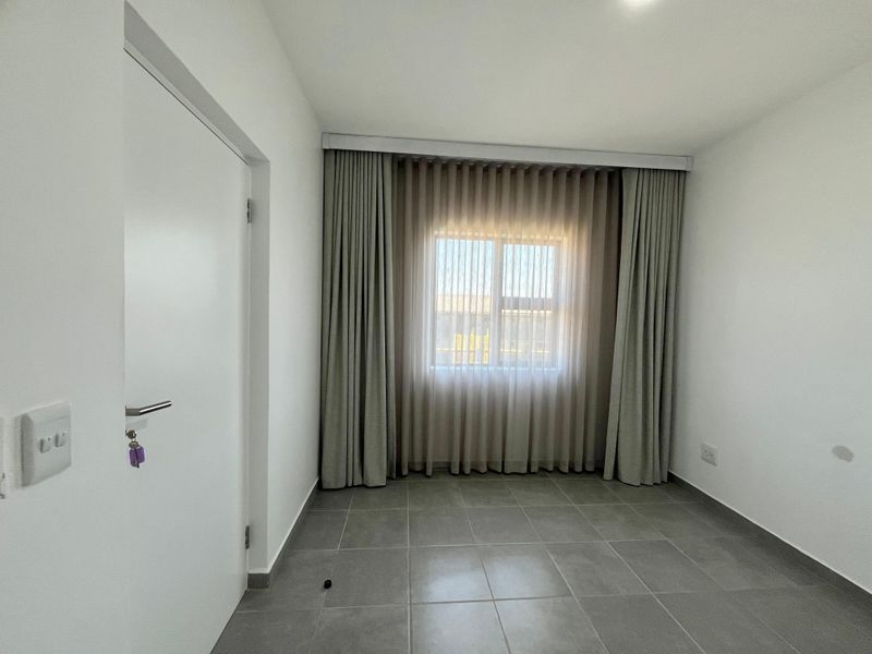 A clean, empty bedroom featuring neutral tiled flooring, white walls, and floor-to-ceiling curtains over a central window.