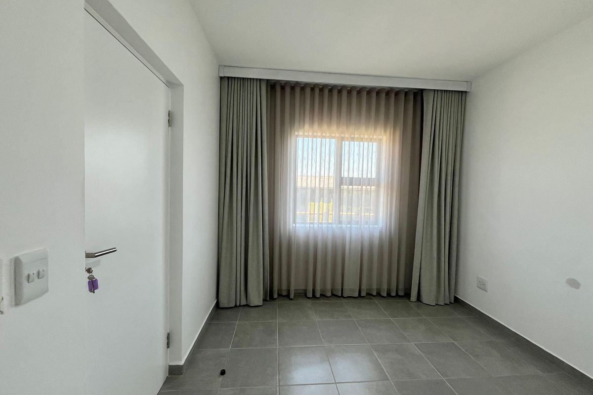 A clean, empty bedroom featuring neutral tiled flooring, white walls, and floor-to-ceiling curtains over a central window.