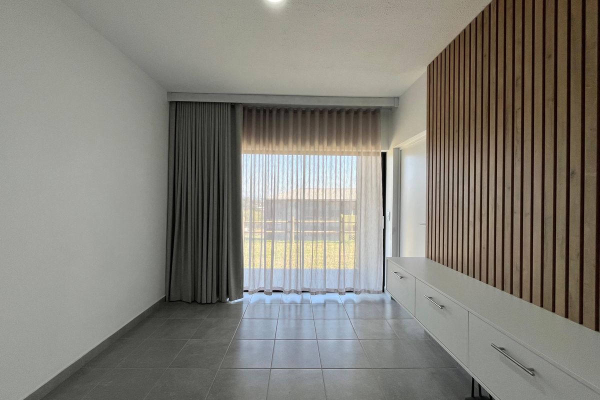 A bright, modern living room featuring large format floor tiles, a stylish timber slat feature wall, and built-in storage cabinetry.