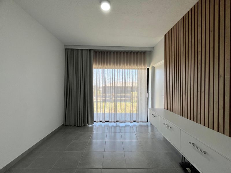 A bright, modern living room featuring large format floor tiles, a stylish timber slat feature wall, and built-in storage cabinetry.