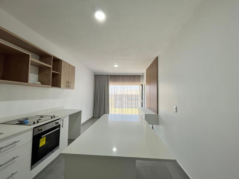 Modern open-plan kitchen and living area featuring a central island, built-in oven, gas cooktop, and elegant slatted wood wall detailing.