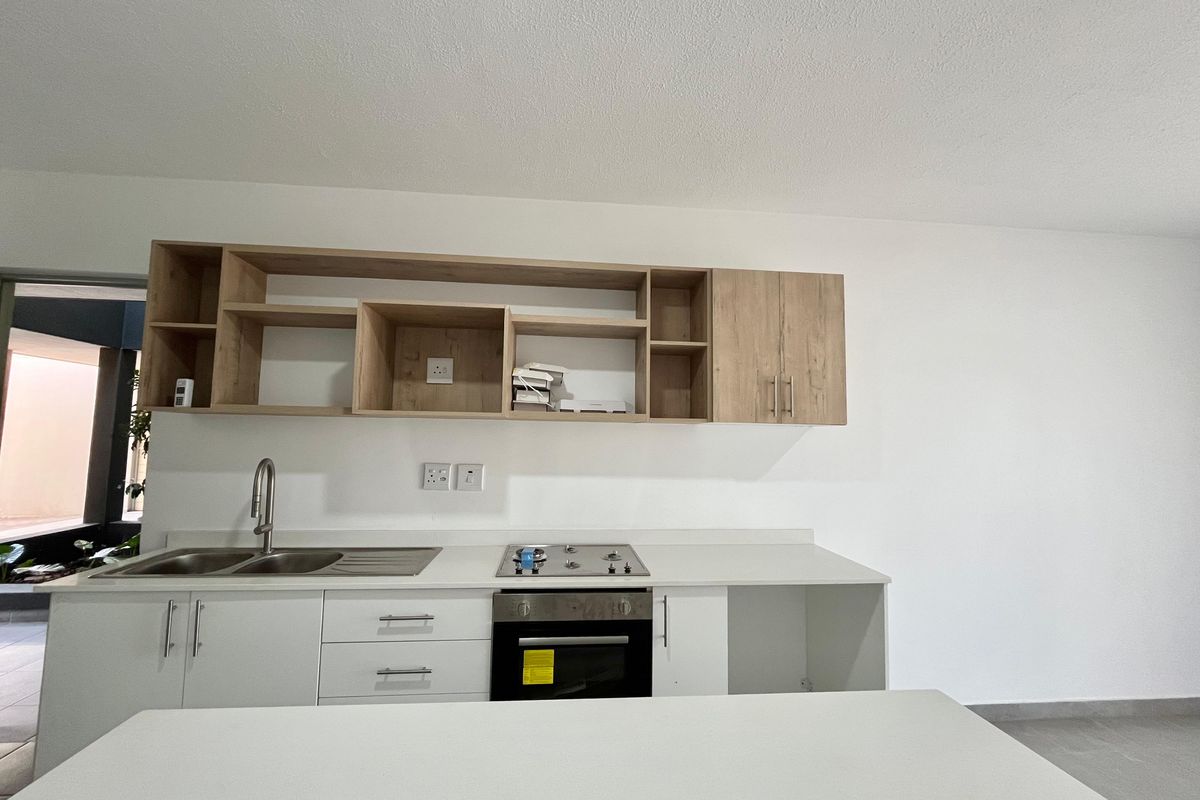 A modern, clean kitchen featuring light wood cabinetry, white stone countertops, a built-in oven, gas hob, and a stainless steel sink.