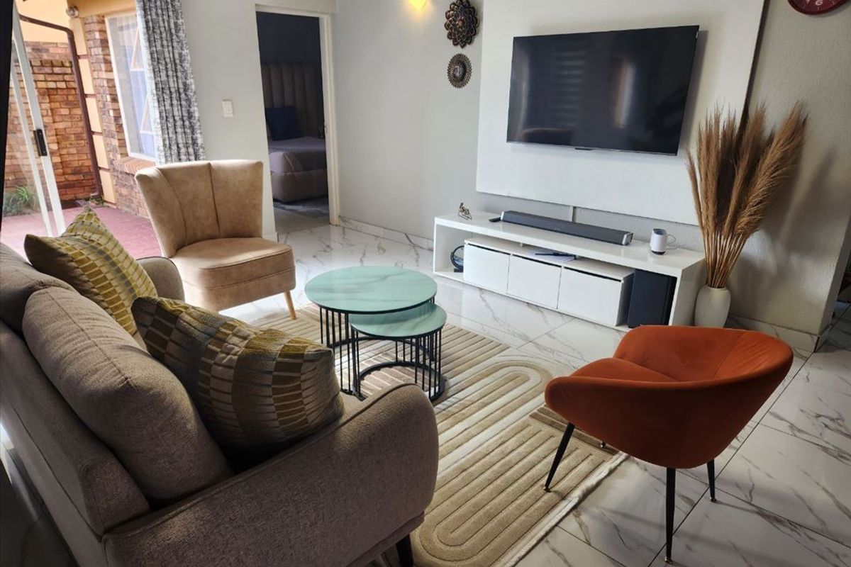 A well-maintained living room featuring modern marble-look floor tiles, a built-in media wall, and direct access to an outdoor patio area.