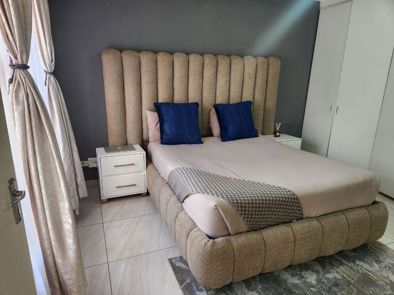 A well-maintained bedroom featuring neutral tiled flooring, a dark accent wall, and integrated built-in cupboards for storage.