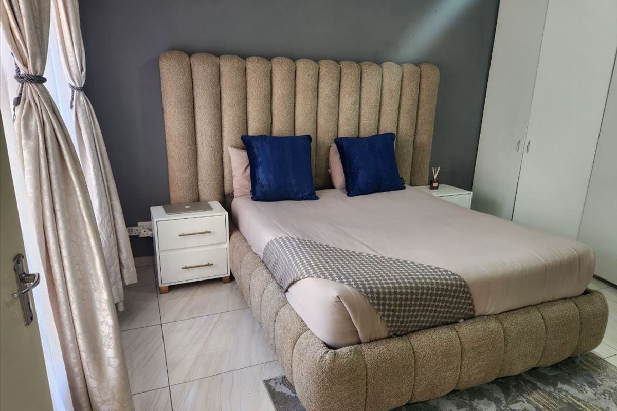 A well-maintained bedroom featuring neutral tiled flooring, a dark accent wall, and integrated built-in cupboards for storage.
