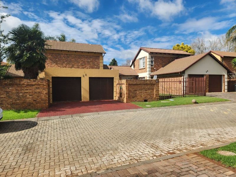 Front exterior view of a townhouse featuring a double garage, brick facade, and paved driveway within a residential complex.