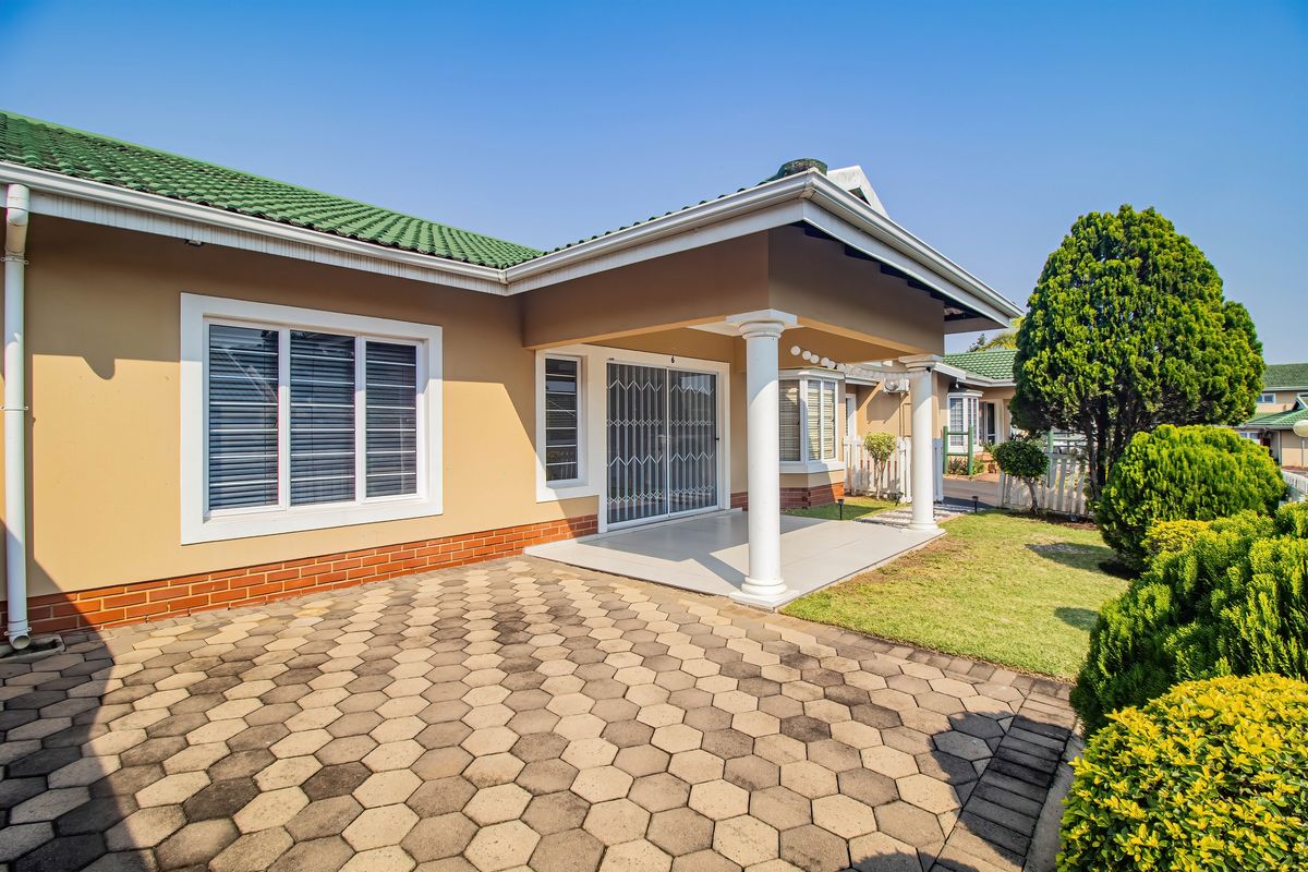 A well-maintained rear exterior view of the townhouse featuring a covered patio, paved area, and green garden space.