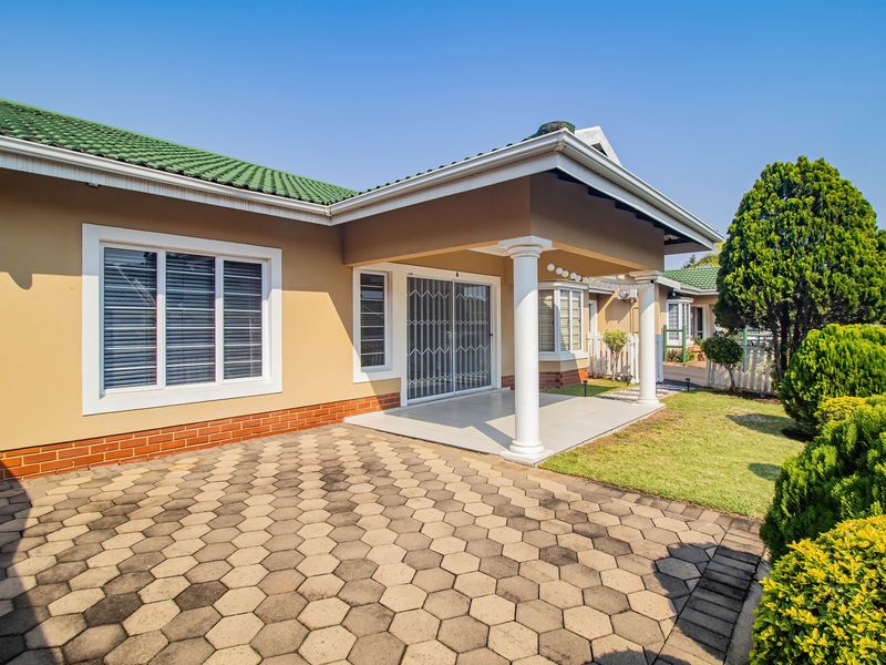 A well-maintained rear exterior view of the townhouse featuring a covered patio, paved area, and green garden space.