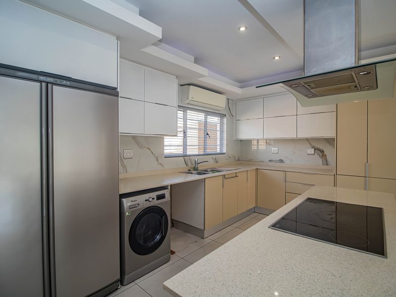 Modern kitchen featuring sleek white and neutral cabinetry, stone countertops, marble-look backsplash, integrated hob, and stainless steel extractor fan.