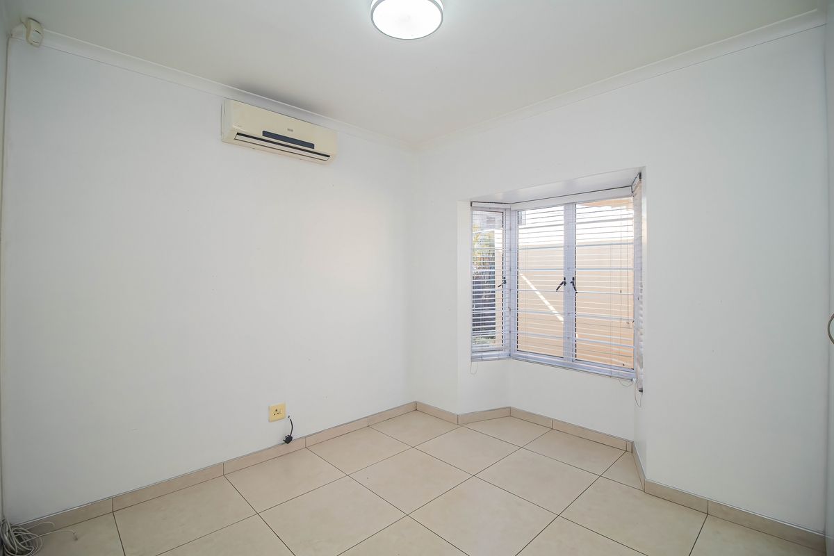 A bright, empty bedroom featuring tiled flooring, a bay window with venetian blinds, and a wall-mounted air conditioning unit.