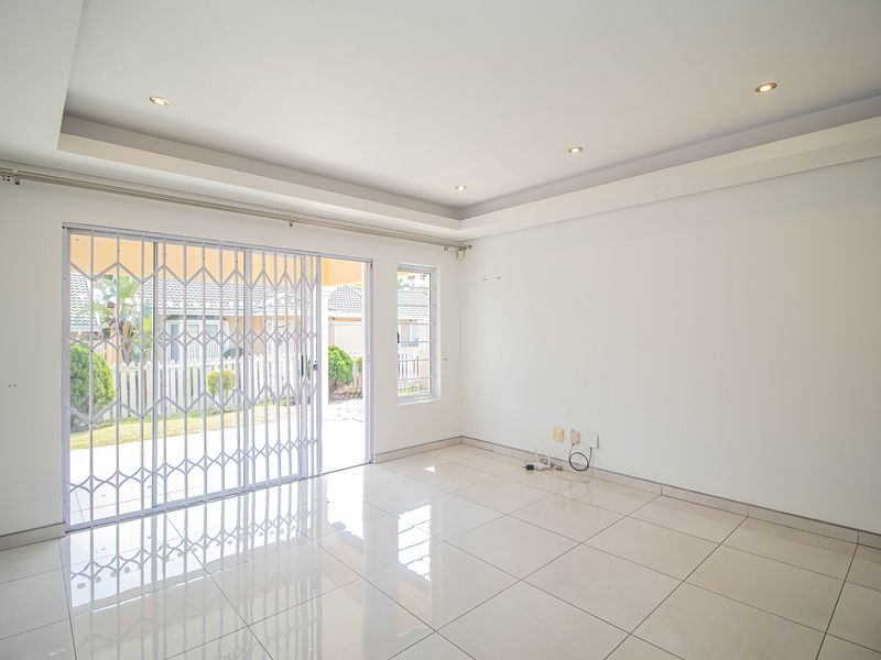 Bright and spacious living area featuring polished tile flooring, recessed ceiling lighting, and a sliding glass door with a security gate leading outdoors.