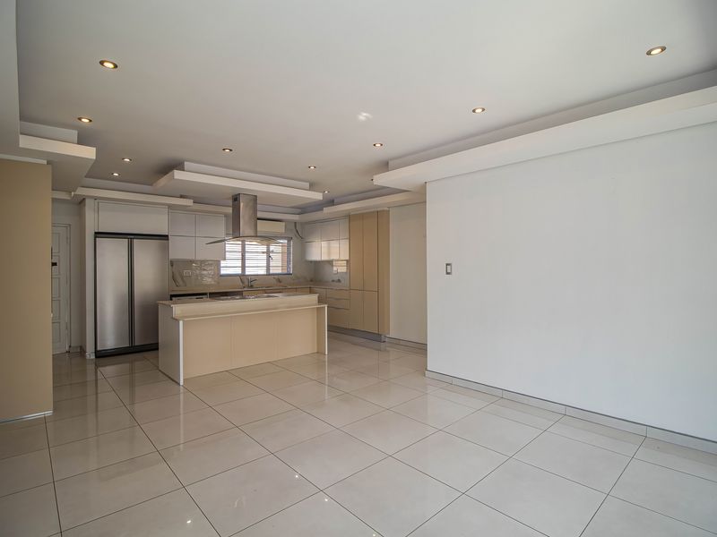 Spacious open-plan kitchen and living area featuring modern cabinetry, a central island, recessed lighting, and neutral tiled flooring throughout.