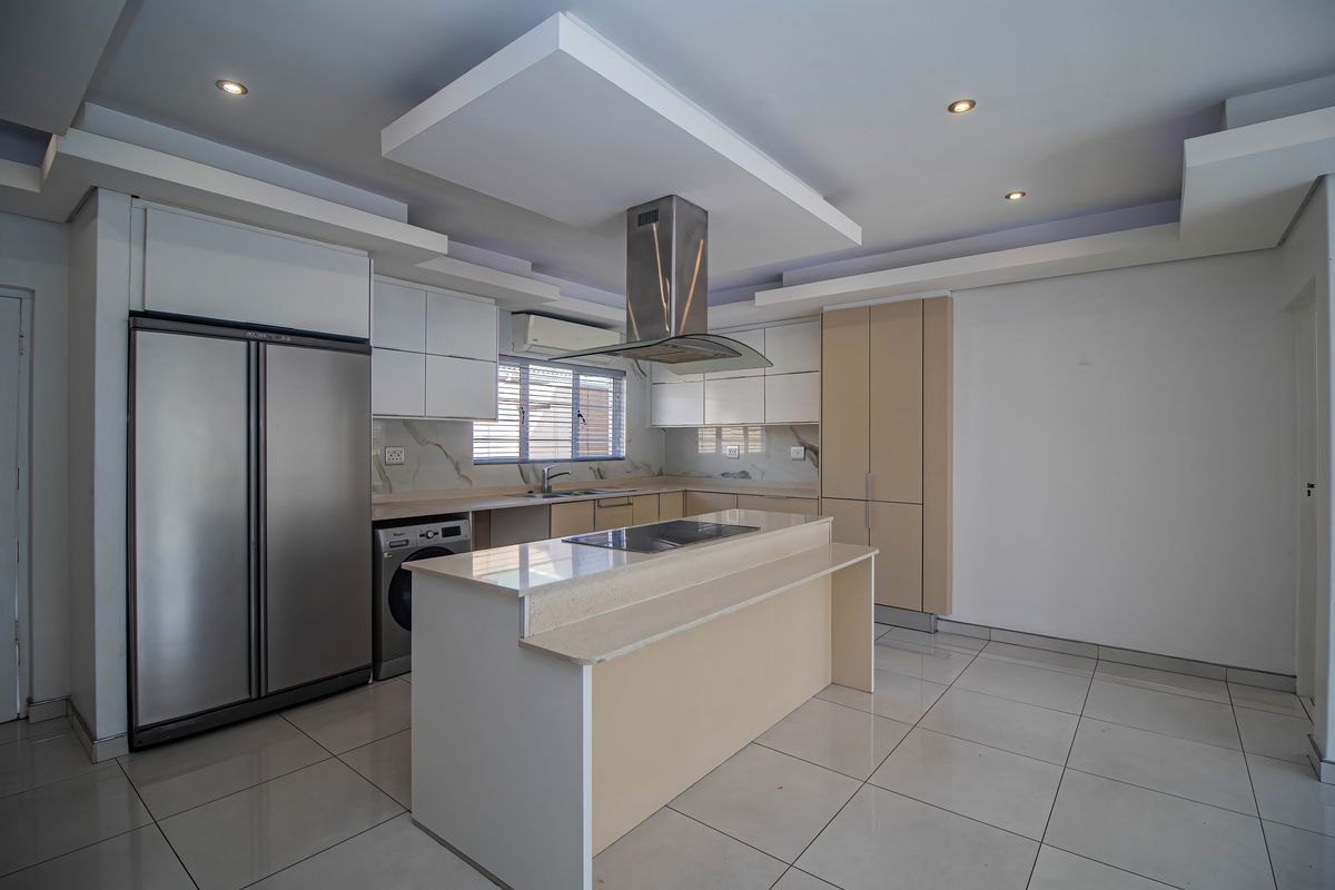 Modern kitchen featuring a central island, built-in appliances, sleek cabinetry, stone countertops, and recessed lighting in a spacious, open-plan layout.