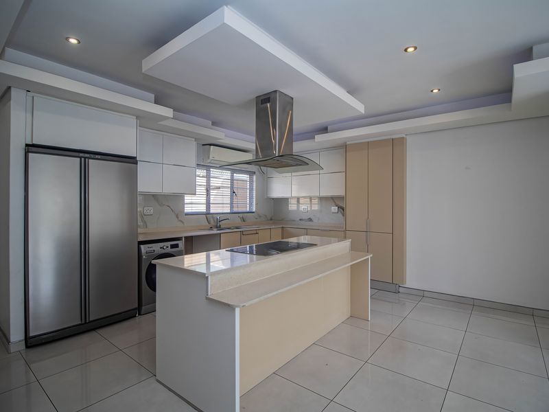 Modern kitchen featuring a central island, built-in appliances, sleek cabinetry, stone countertops, and recessed lighting in a spacious, open-plan layout.