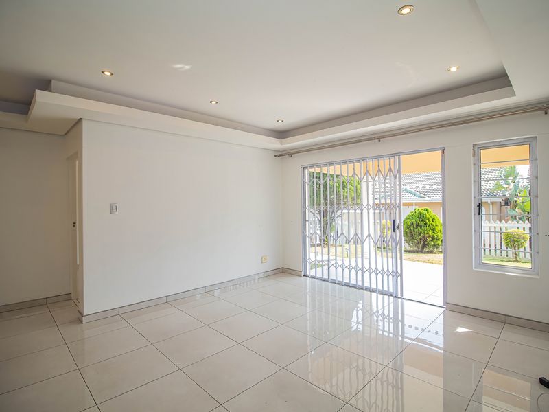 Bright and spacious living area featuring neutral tiled flooring, recessed ceiling lighting, and a sliding glass door with security gate leading to the exterior.