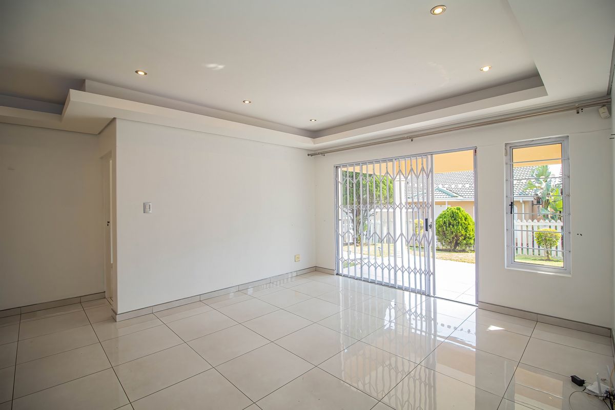 Bright and spacious living area featuring neutral tiled flooring, recessed ceiling lighting, and a sliding glass door with security gate leading to the exterior.