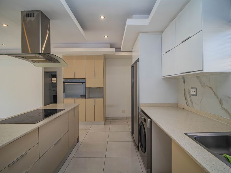 Modern kitchen featuring stone countertops, built-in oven, hob, extractor fan, and ample cabinetry with tiled flooring and recessed lighting.
