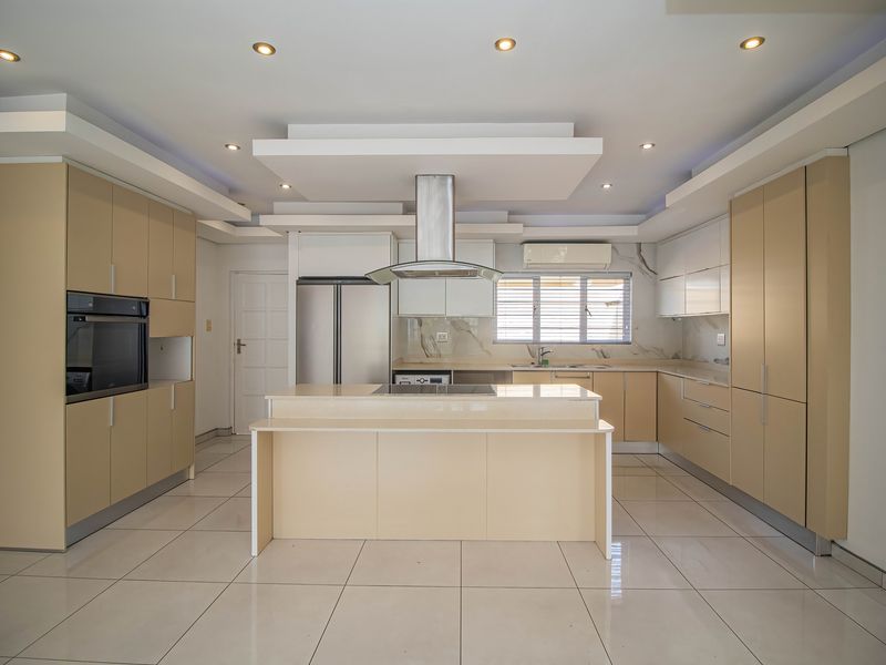 Modern kitchen featuring a central island, built-in oven, extractor fan, stone countertops, and ample cabinetry with recessed lighting and a drop ceiling design.