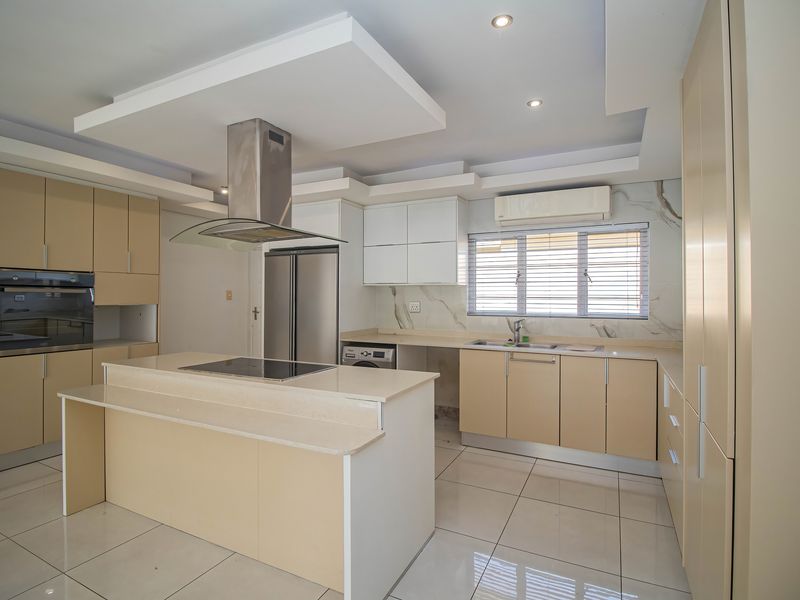 Modern kitchen featuring a central island, built-in oven, extractor fan, stone countertops, and ample cabinetry with sleek tiled flooring.