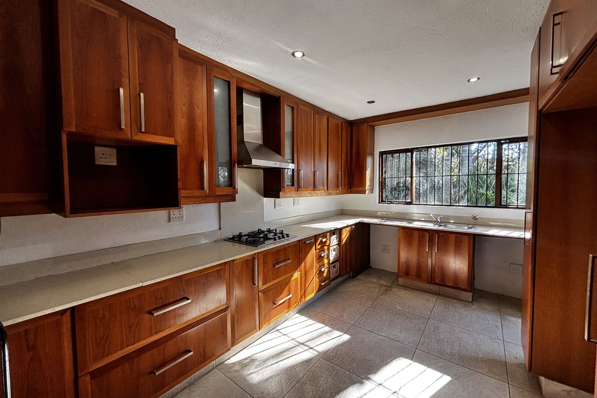 A functional kitchen featuring warm-toned wooden cabinetry, stone countertops, a gas hob with extractor, and tiled flooring, offering a classic layout.