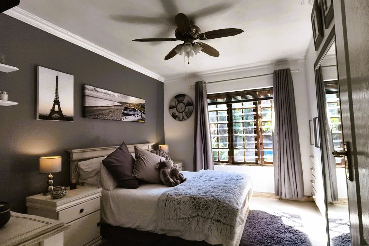 A well-maintained bedroom featuring crown molding, a ceiling fan, and large wooden-framed windows that allow for natural light.